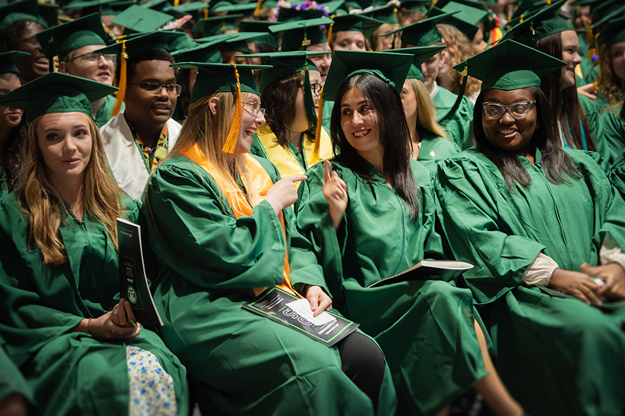 Gemini said A smiling student receives blue and yellow graduation cords from a faculty member during a ceremony featuring colorful balloons and academic banners.